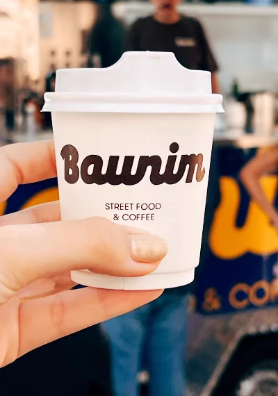 Copo de café quente da Baunim na mão de uma cliente