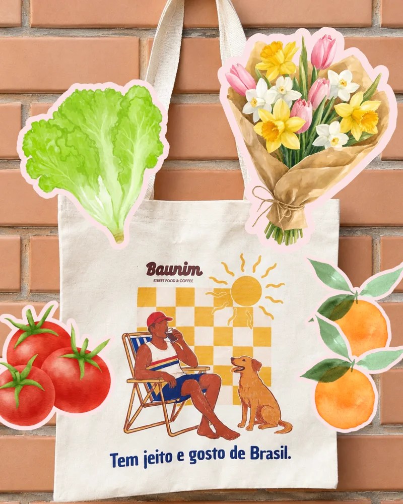 Ecobag da Baunim pendurada numa parede de tijolinhos, cercada de alface, tomates, laranjas e flores