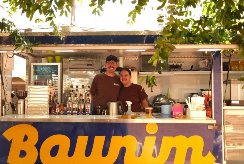 A janela do trailer aberta, com a equipe da Baunim atrás do balcão e o letreiro amarelo